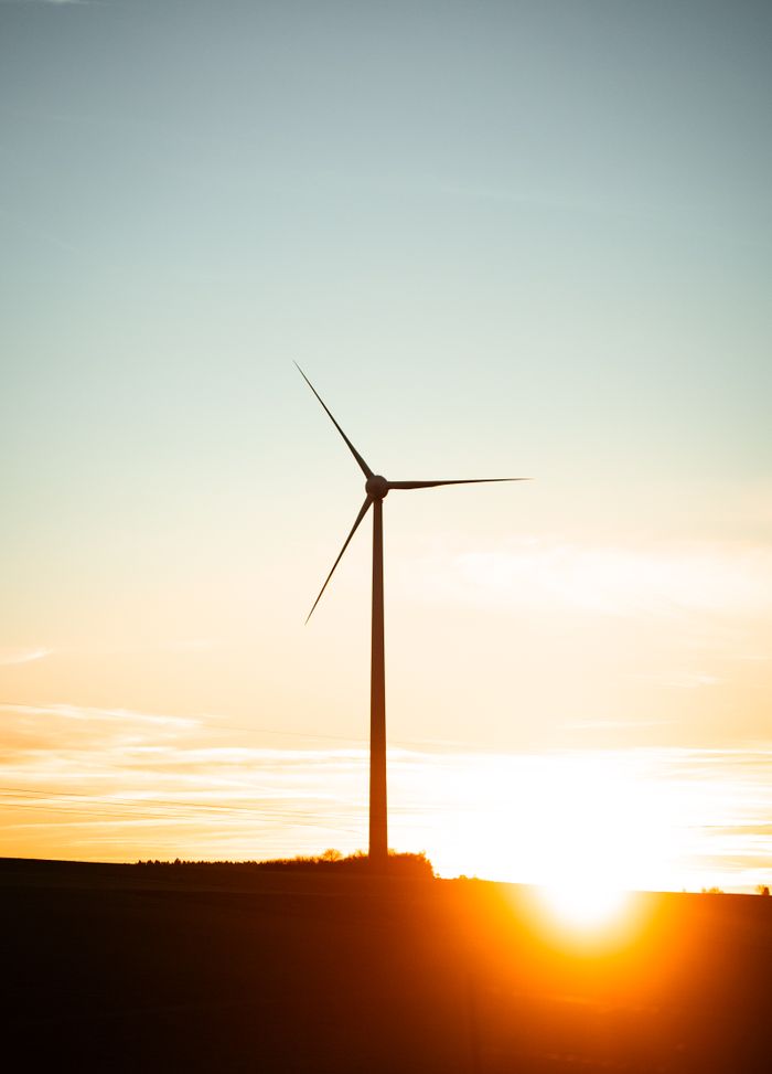 About A scenic view of a wind turbine silhouetted against a vibrant sunset in rural Austria.